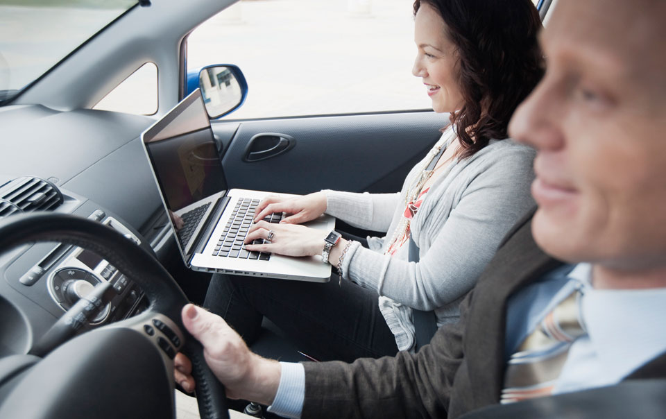 Professionals in car and passenger typing on laptop