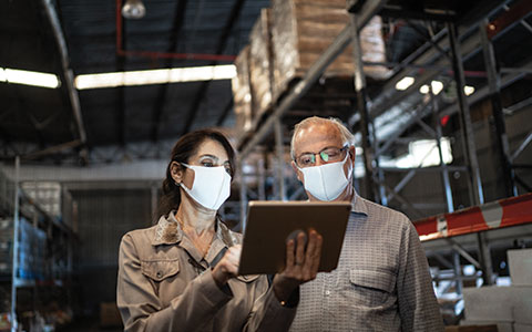 一男一女戴着面具在仓库里看平板电脑。正确的商业保险范围以保护您的公司