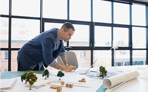 男人站在办公桌前工作在笔记本电脑上，如何选择一个专业的责任保险政策为您的设计公司