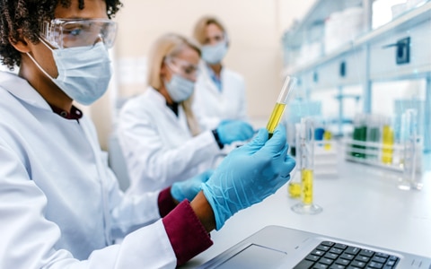 lab technician looking at test tubes and a laptop, Risks Facing Pharmaceutical Companies, From Trial to Commercialization