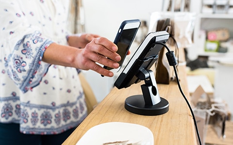 Image of person holding their phone to a retail payment device. Accpepting Mobile Payments for Your Small Business