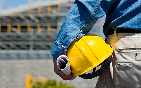 man holding yellow hardhat in front of construction site