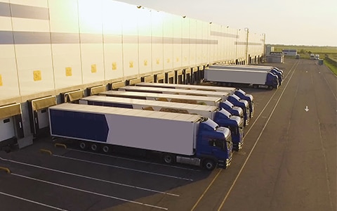 货运卡车排列在装载/卸载的建筑物上，运输经纪人模型的演变带来了新的风险
