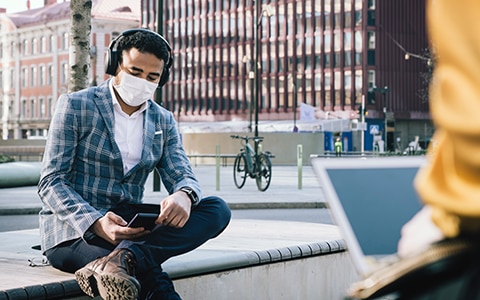 一名男子戴着口罩坐在城市长椅上看手机，《支持新冠肺炎后工作场所的心理健康》