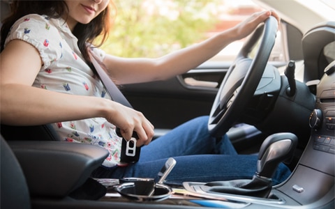 一位女士坐在她的汽车方向盘后面，把她的手机放在中控台，7个常见的车祸和如何避免它们